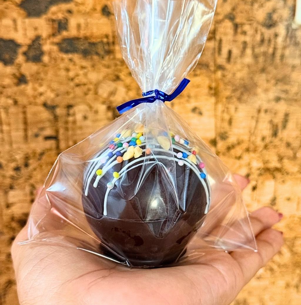 ChocoBomba de chocolate negro decorada con hilos blancos y lluvia de colores, en su bolsita con lazo azul